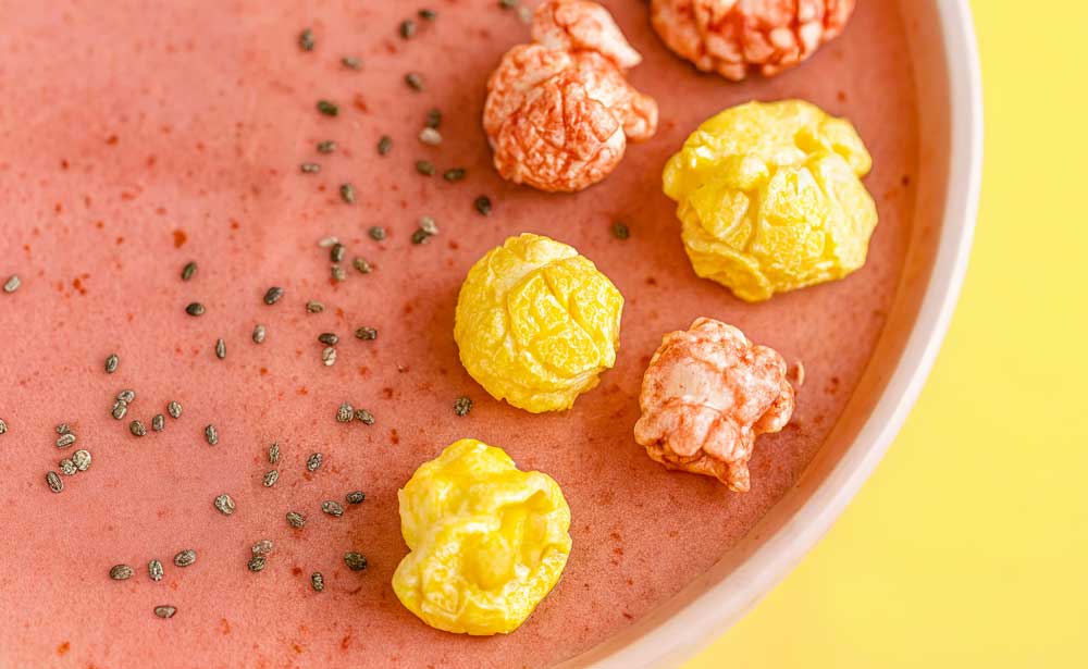 Delicious Strawberry & Banana Pop Yum Super Smoothie Bowl recipe topped with colorful popcorn.