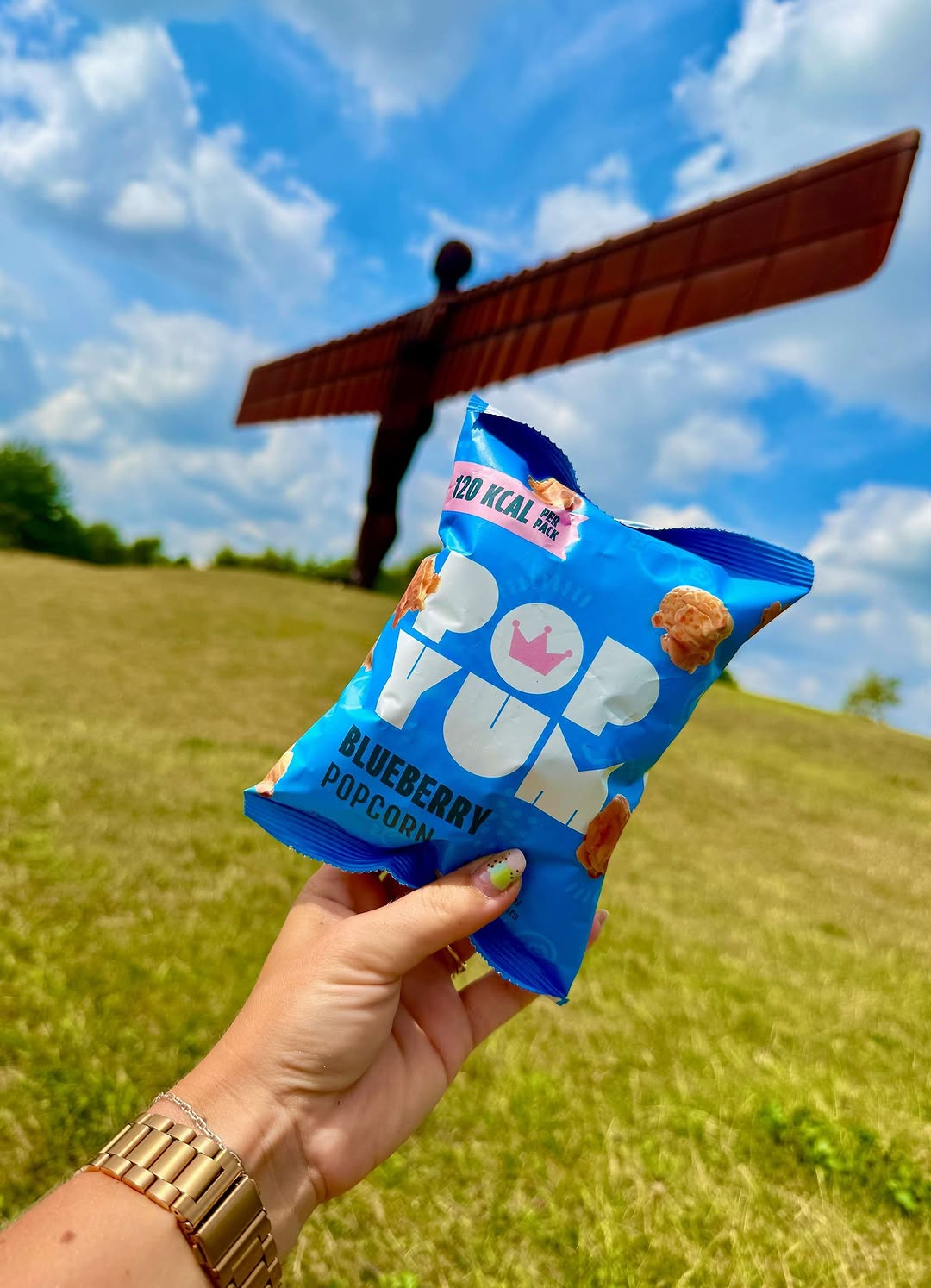 Blue Pop Yum blueberry popcorn packet held in front of the Angel of the North sculpture.