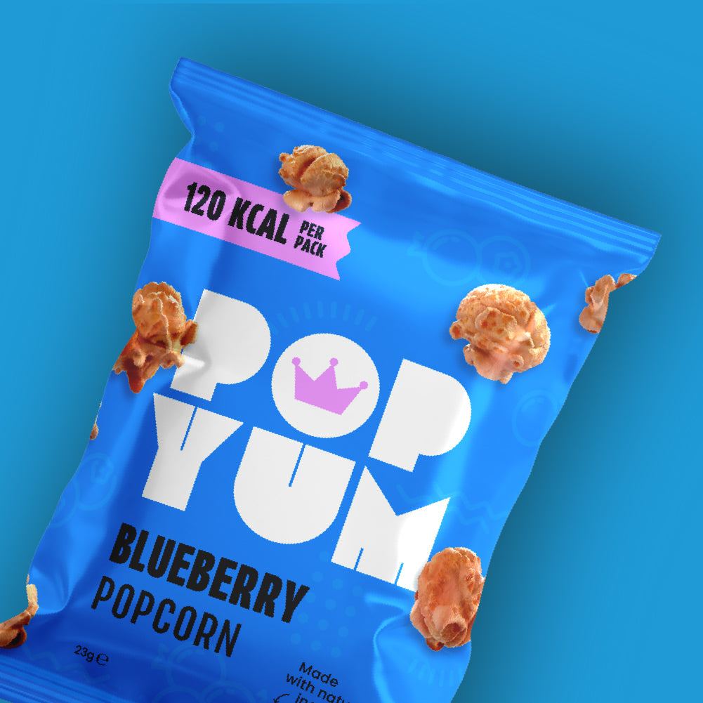 Blue packet of Pop Yum vegan blueberry popcorn on a blue background. 120 kcal per pack is also displayed.