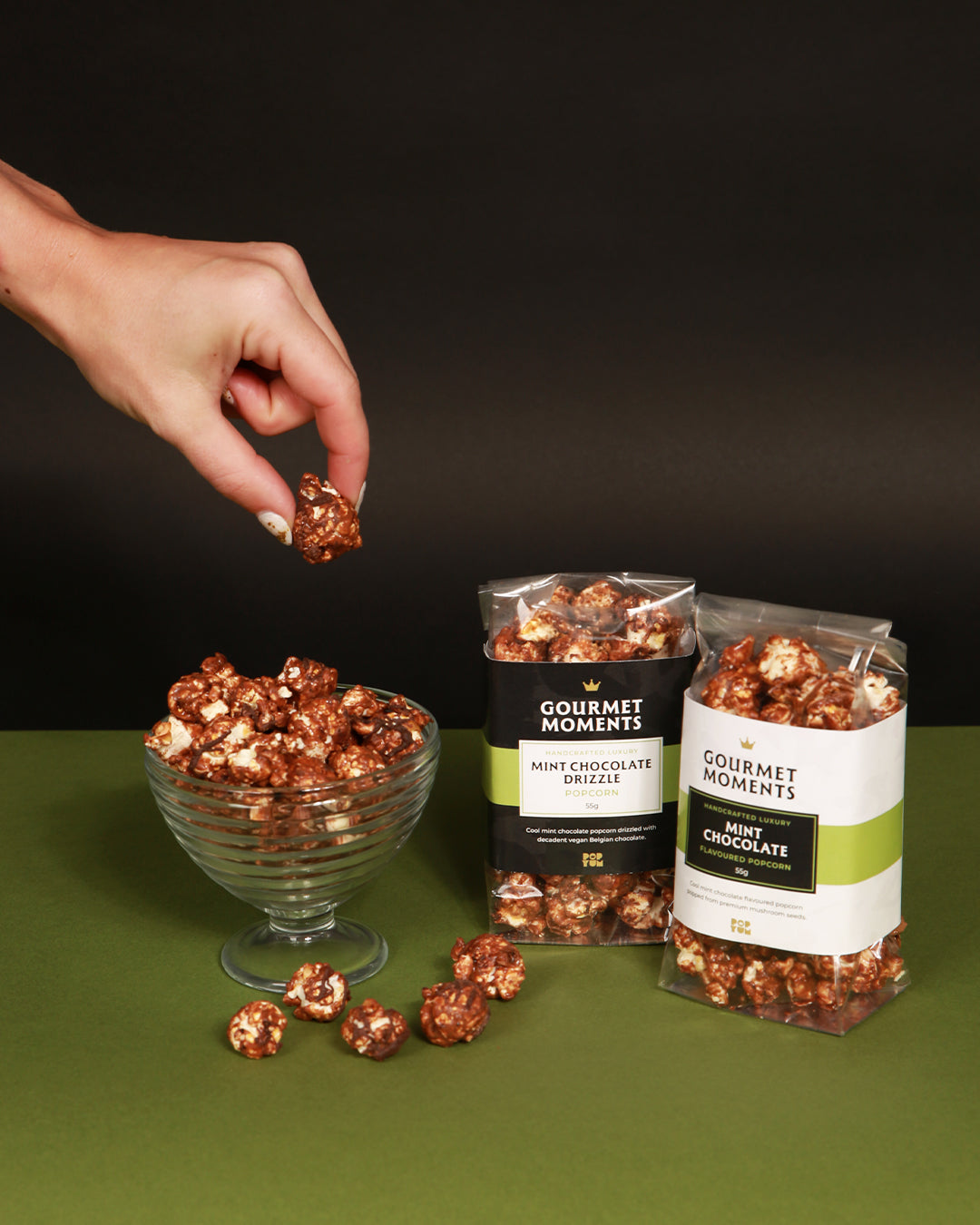 Gourmet Moments Mint Chocolate popcorn packets, in plain & chocolate-drizzle, on a green surface against a black background
