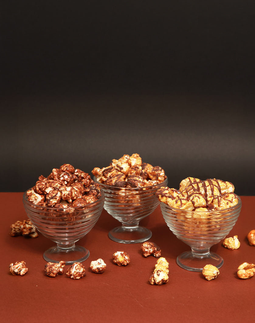 Three glass bowls filled with gourmet popcorn on a dark background