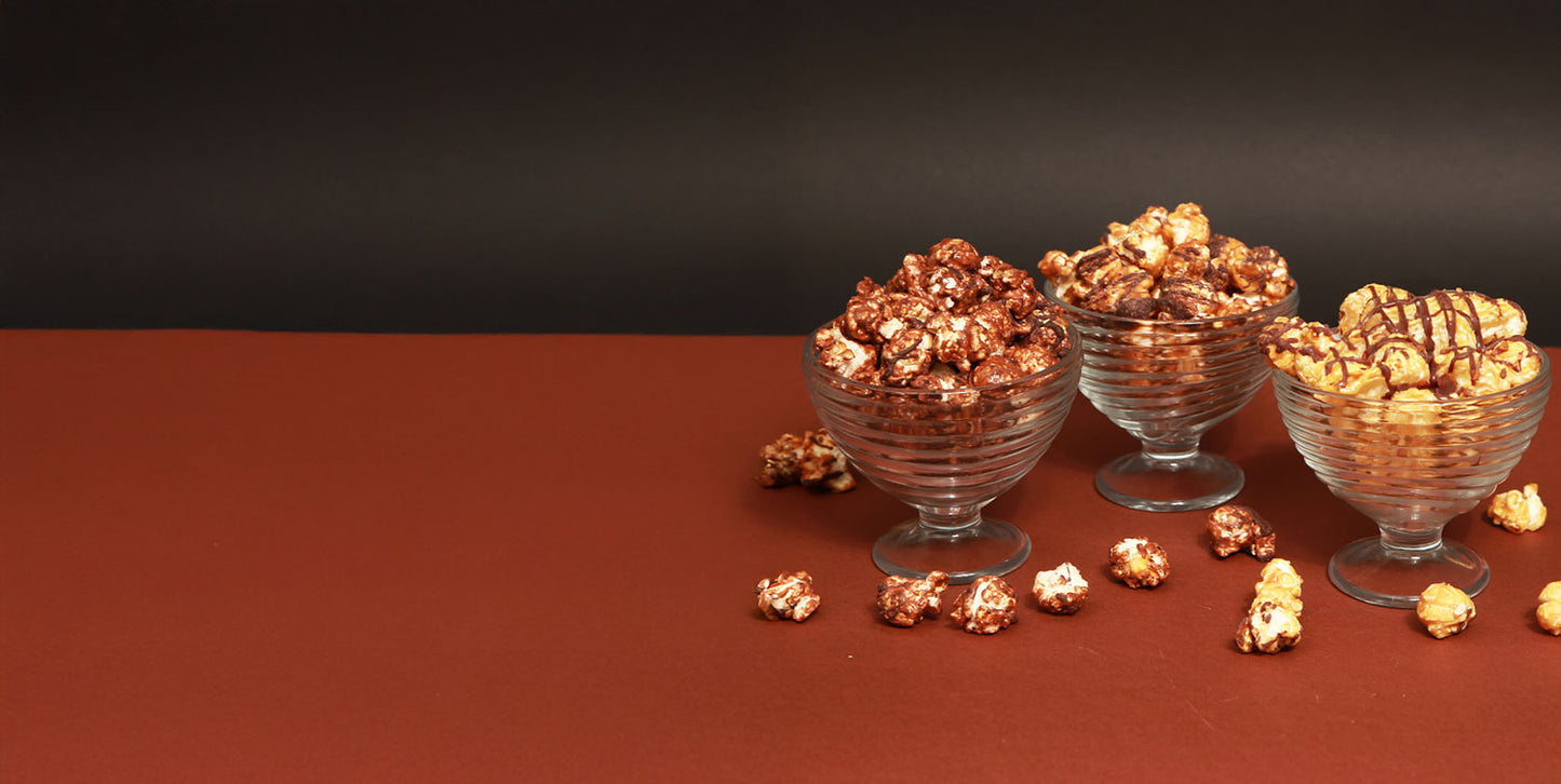 Glass bowls filled with gourmet popcorn on a brown surface with a dark background