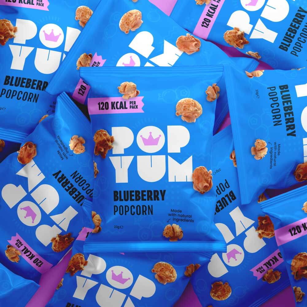 A pile of Pop Yum blueberry-flavoured popcorn packets on a purple background. Low-calorie, gluten-free popcorn pile.
