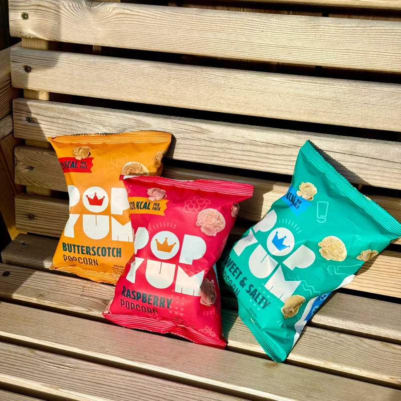 Pop Yum sweet & salty, butterscotch and raspberry vegan popcorn treats on an outdoor wooden bench surface.