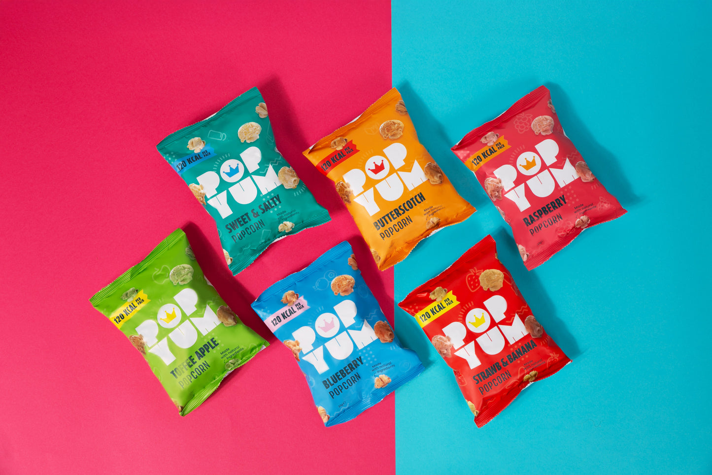 Colourful Pop Yum popcorn packets on a two-tone pink and blue background. 120 calories per pack is displayed on each packet.