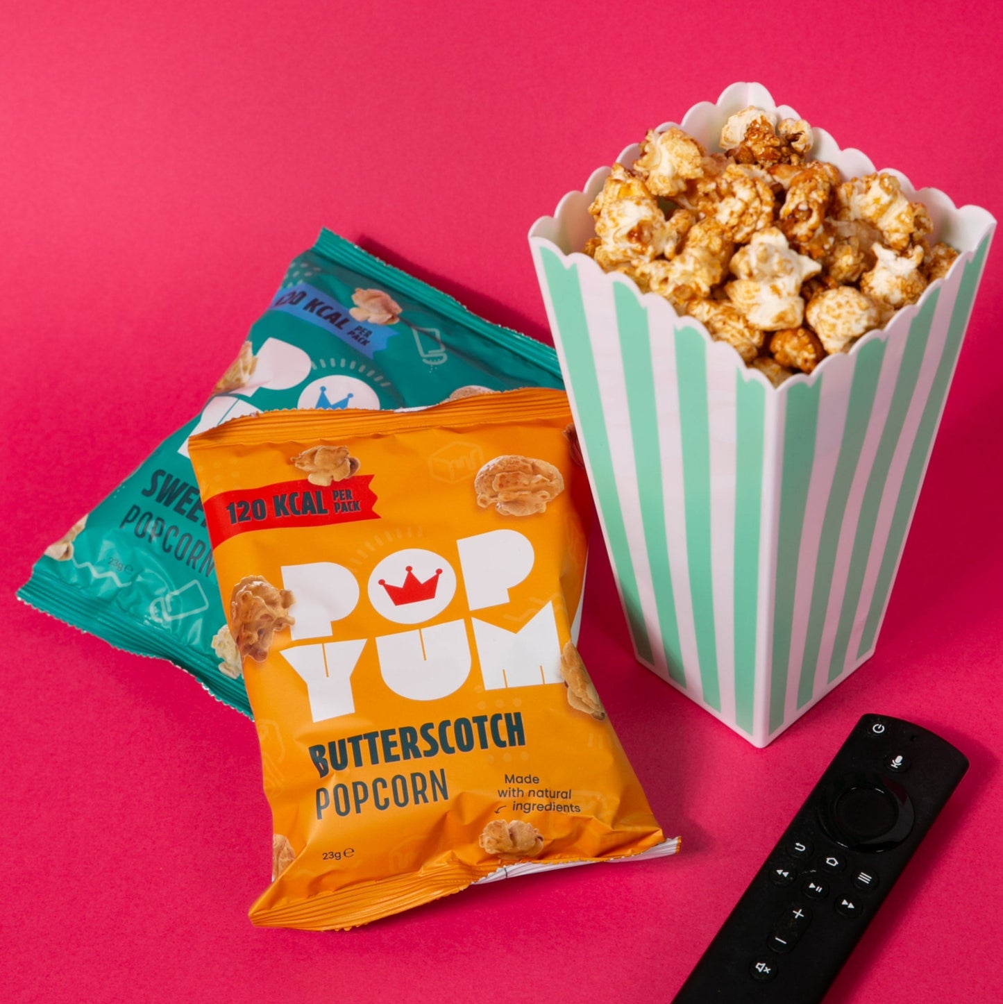 Popcorn packets and striped container on a pink background