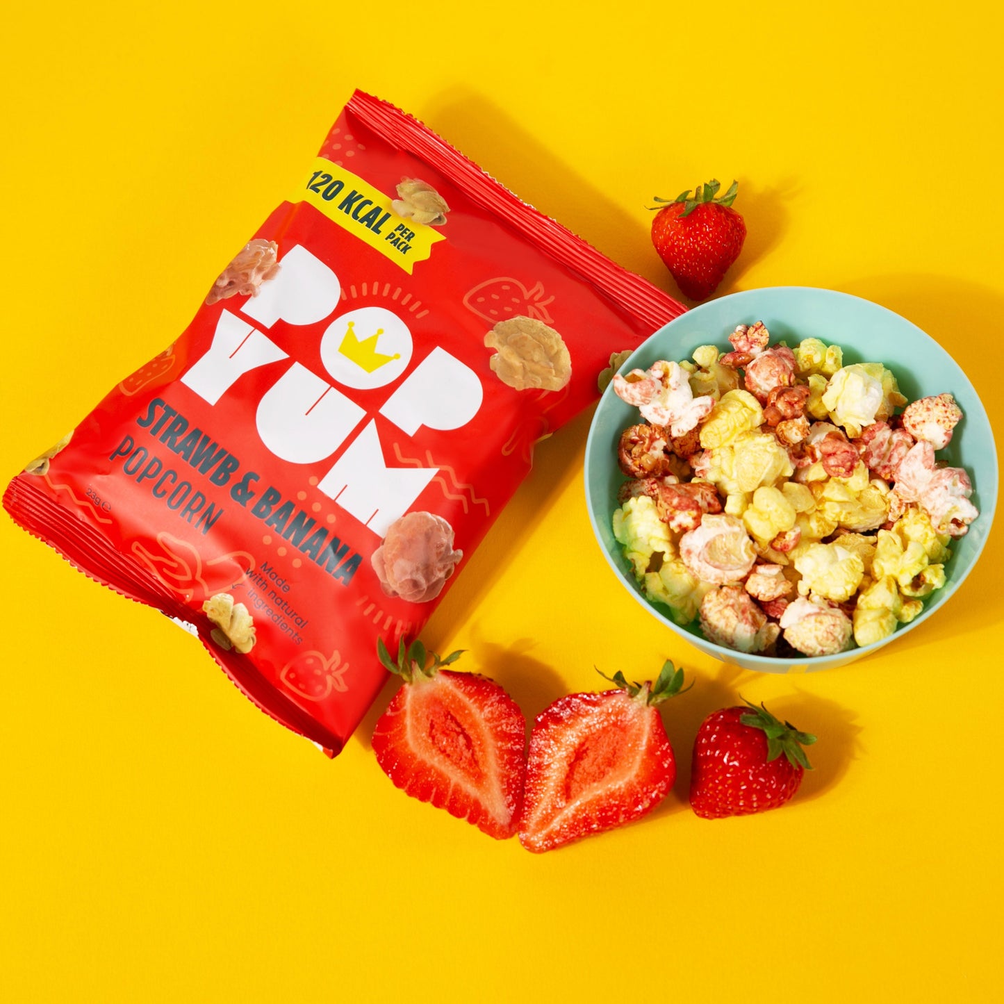 Red Pop Yum strawberry and banana popcorn packet with a bowl of popcorn and strawberries on a yellow background